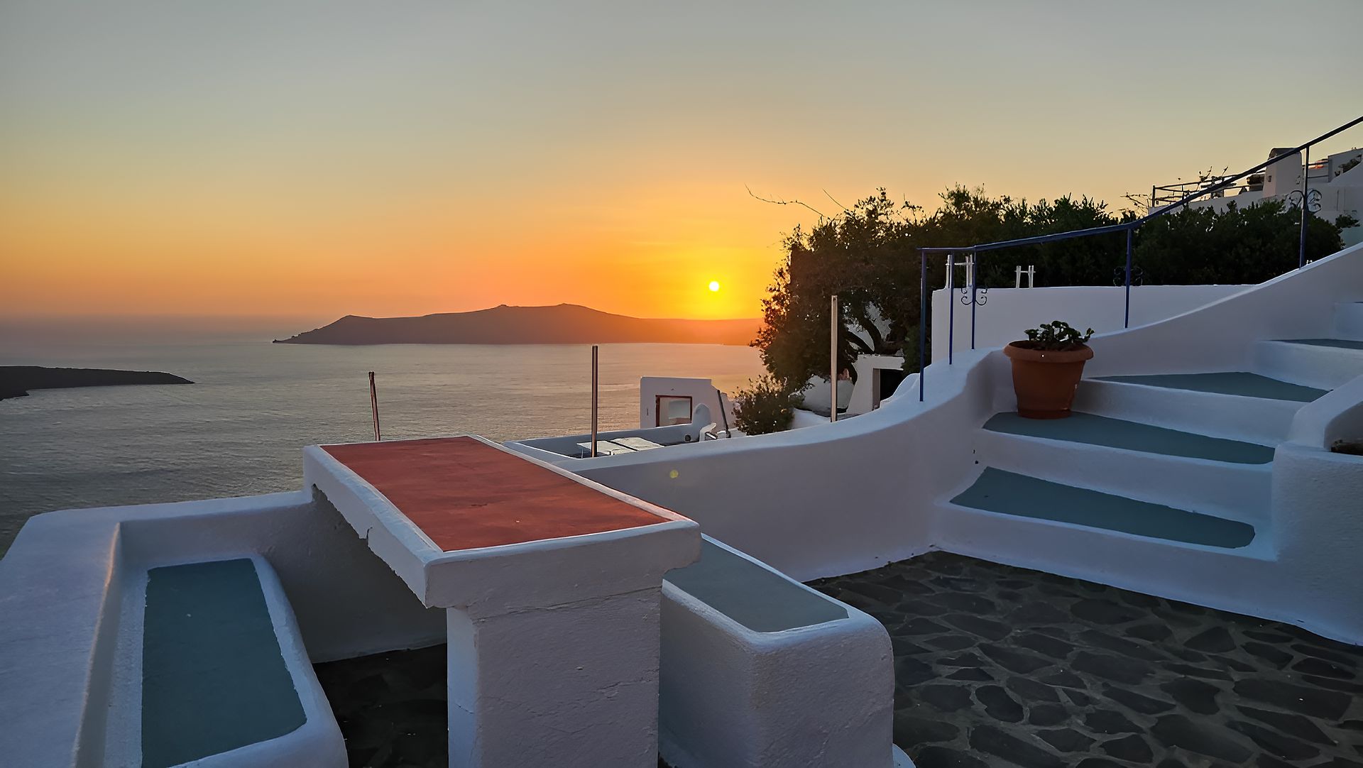 A charming Santorini cave house with whitewashed walls, a cozy terrace overlooking the Aegean Sea, and a soft glow from the sunset.