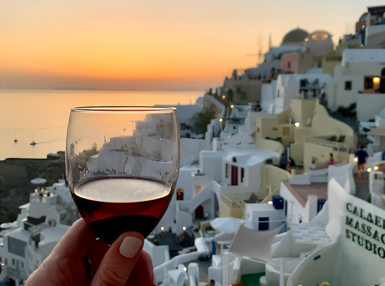 A breathtaking sunset over Santorini, painting the sky in shades of orange and pink, as a wine glass reflects the golden hues.