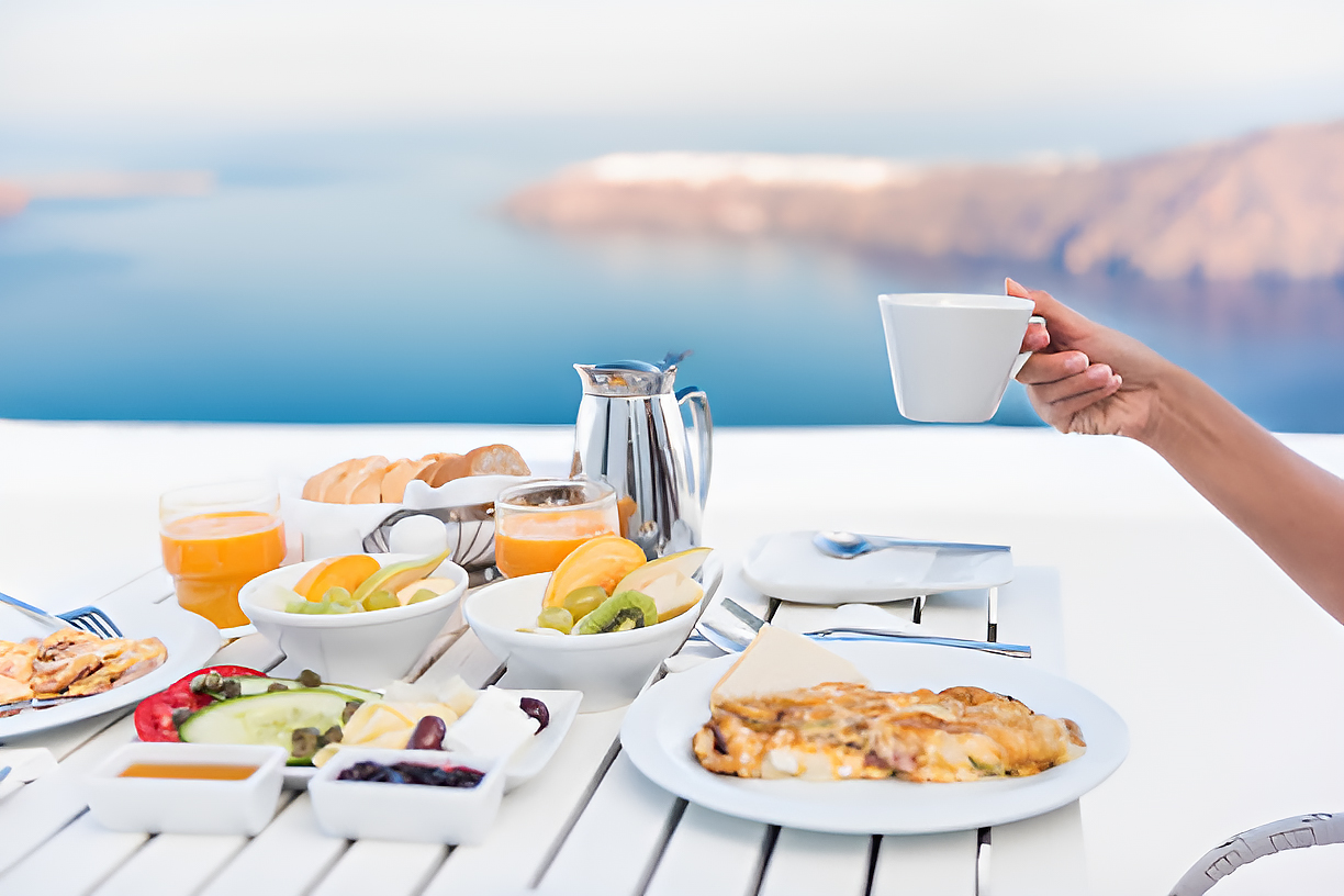 A quiet Santorini morning with a cup of coffee and a journal resting on a sunlit terrace, overlooking the endless blue Aegean Sea.