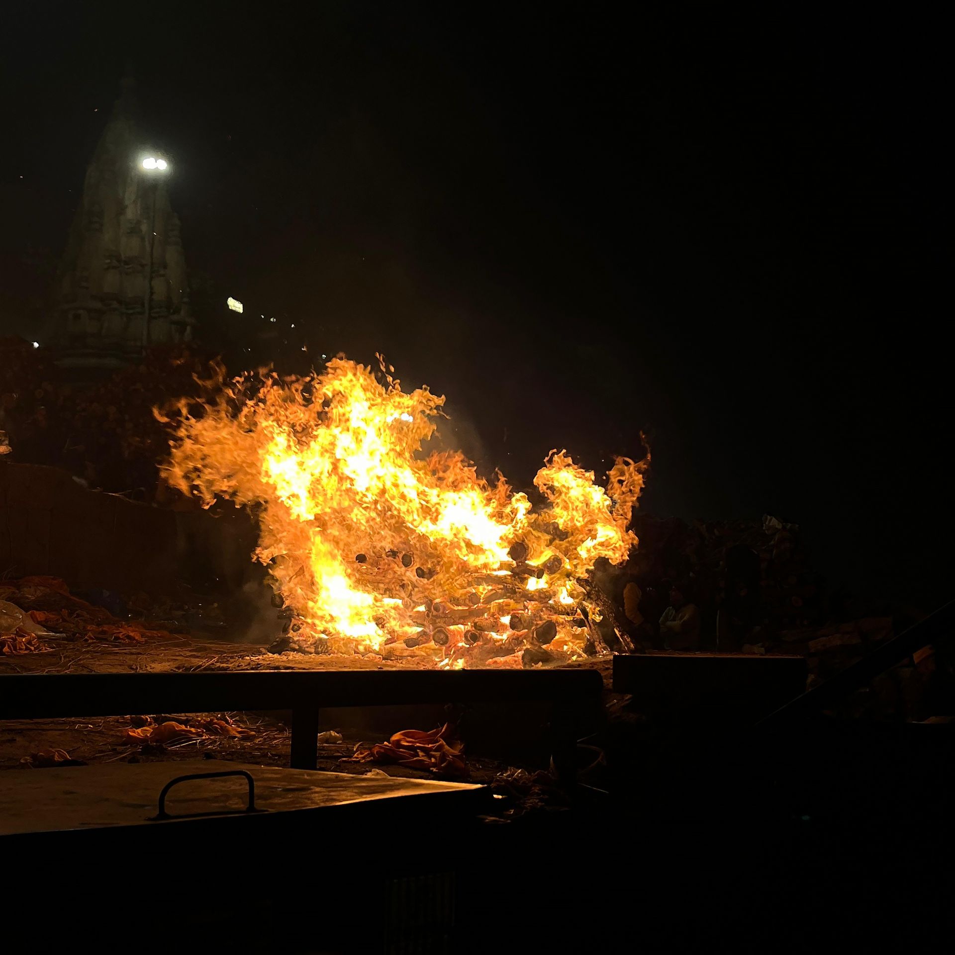 A cremation fire burns at Manikarnika Ghat in Varanasi, with flames rising into the night. The sacred site, illuminated by firelight, symbolizes the Hindu belief in moksha, where life and death coexist on the banks of the Ganges.